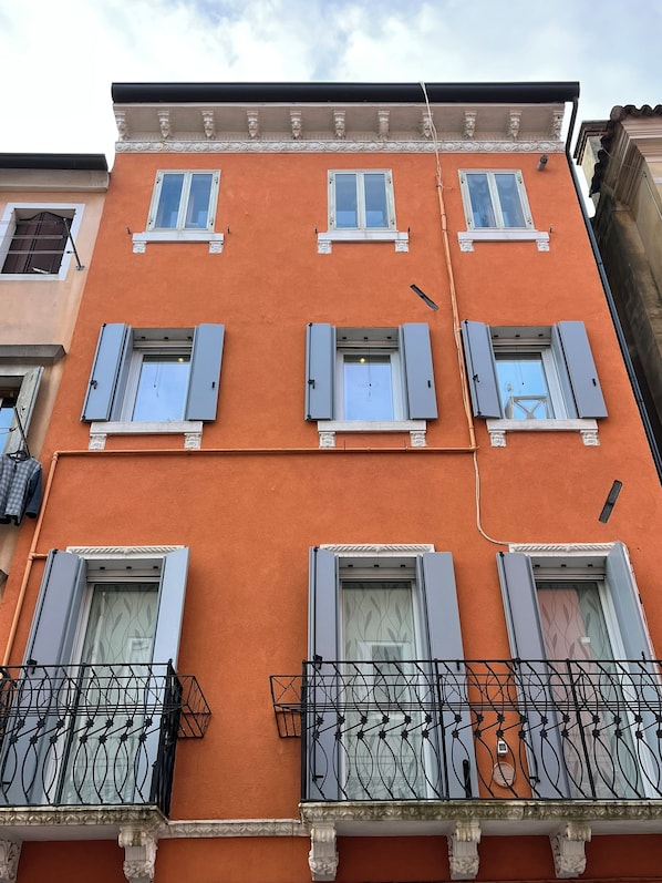 Un edifici de diversos pisos amb balcons, finestres amb persianes i una cornisa decorativa.