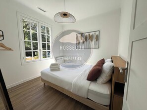 Ein Schlafzimmer mit einem Bett, einem Fenster, einer Hängeleuchte und einem Wandbild.