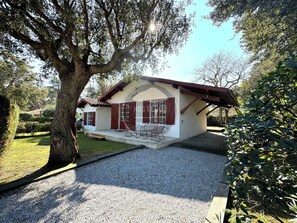 Ein eingeschossiges Haus mit geneigtem Dach, einer Veranda mit Sitzgelegenheiten und einer Auffahrt mit Kies.