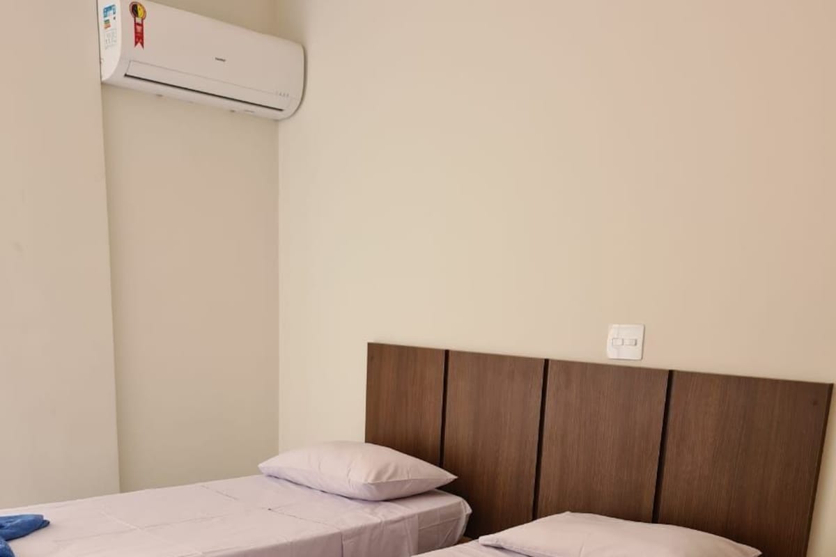 A hotel room with two single beds, a wooden headboard, an air conditioning unit, and a tiled floor.