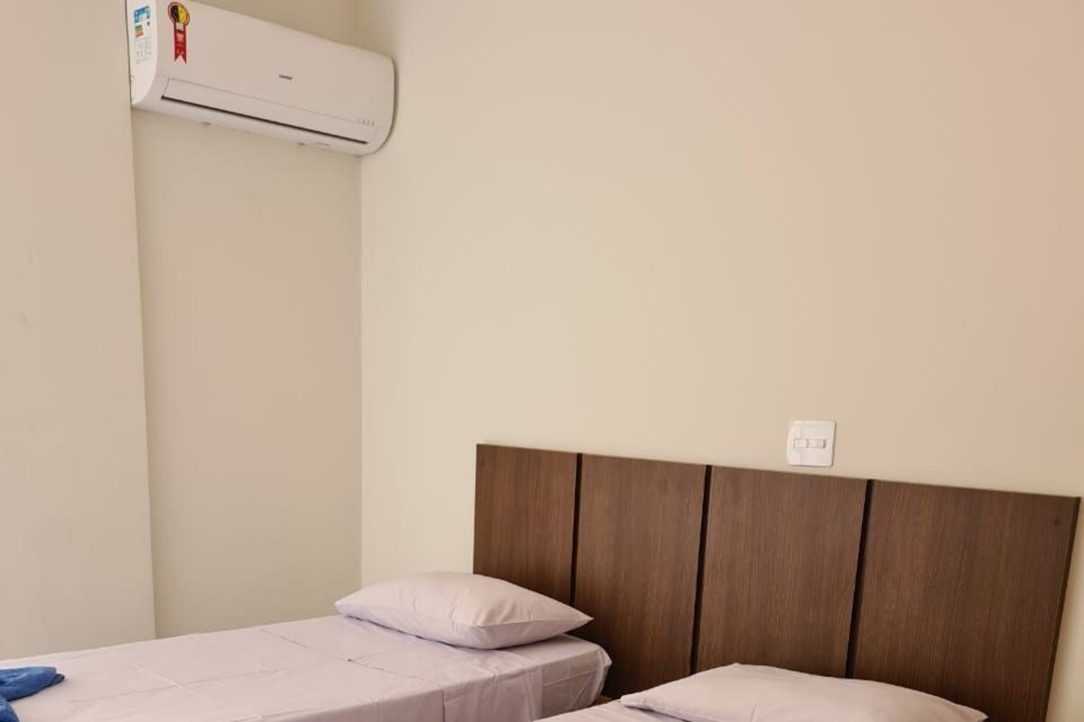 A hotel room with two single beds, a wooden headboard, an air conditioning unit, and a tiled floor.