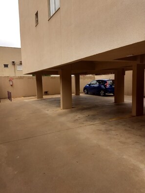 A parking area with a blue car under a building with beige walls and a flat roof. - Edificio Elidio  (São José do Rio Preto)