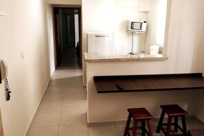A small kitchenette with a microwave, a refrigerator, and a countertop. There are two stools and a small table. - Edificio Elidio  (São José do Rio Preto)