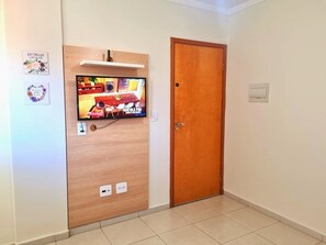 Una habitación con una puerta de madera, un televisor montado en la pared y un pequeño estante sobre la puerta.
