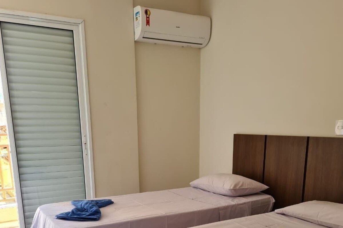 A hotel room with two beds, a window with blinds, an air conditioning unit, and a tiled floor.