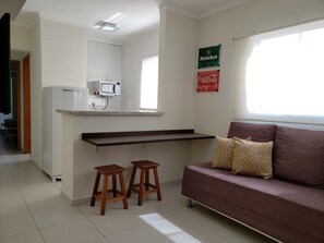 A compact living space with a kitchenette, a sofa, and two stools. - Edificio Elidio  (São José do Rio Preto)