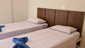 Quarto de hotel com duas camas de solteiro, cabeceira de madeira, ar condicionado e pequena mesa de cabeceira.