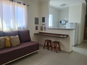 Un espacio habitable con un sofá, dos taburetes, una zona de cocina con microondas y un refrigerador.