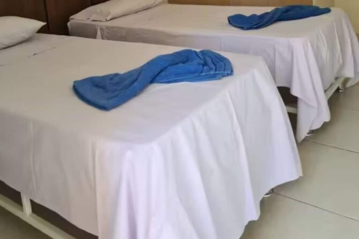 A hotel room with two beds, a wardrobe, and a plain wall.