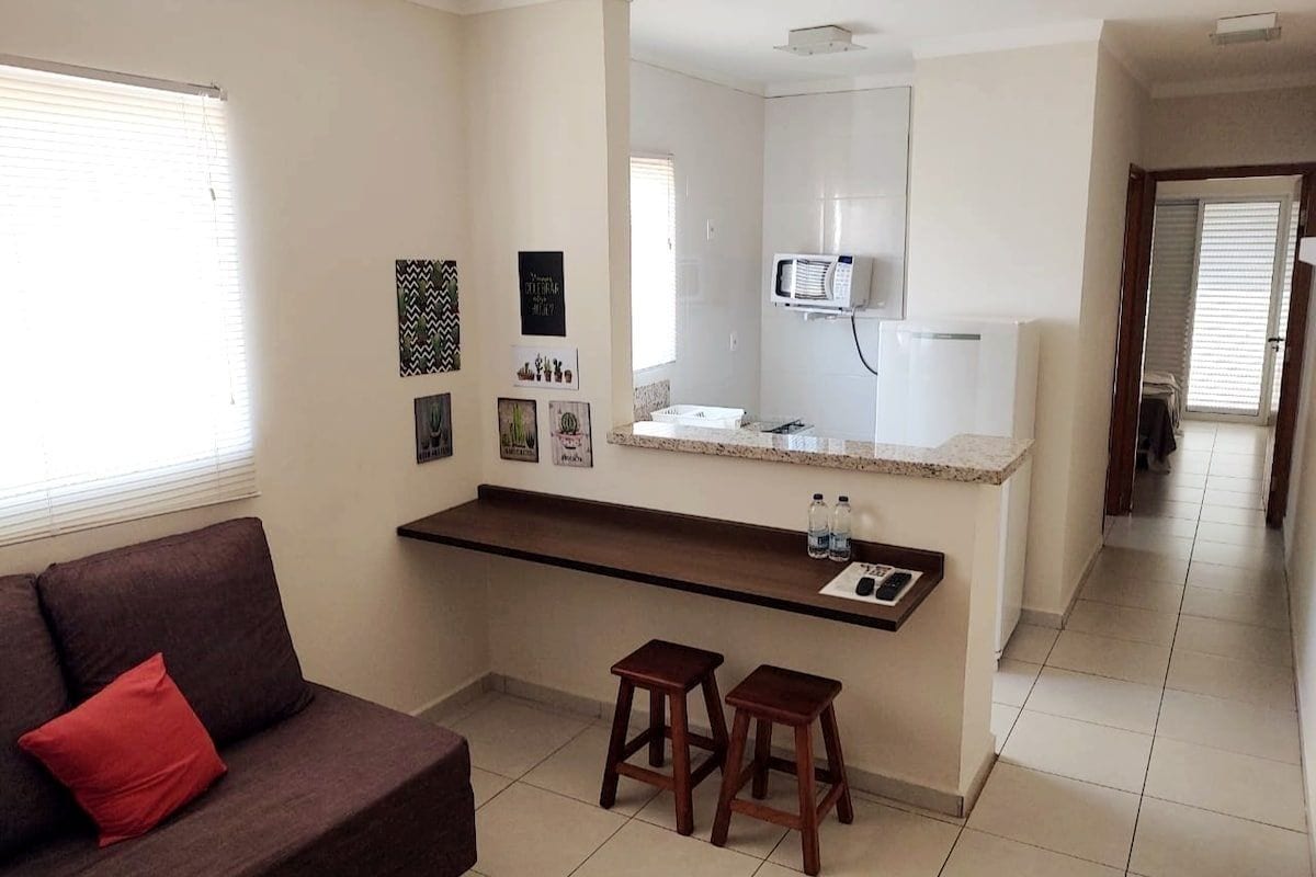 Un espacio habitable compacto con kitchenette, un sofá con un cojín rojo y un pasillo que lleva a otra habitación.