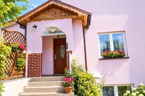 A pink house with a wooden door, a window with flowers, and a brick wall. - Large holiday apartment in Wisełka (Wisełka)