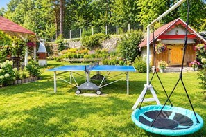 A trampoline, a swing set, and a ping pong table in a garden with a house in the background. - Large holiday apartment in Wisełka (Wisełka)