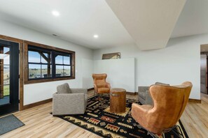 Ein modernes Wohnzimmer mit einem großen Fenster, zwei Ledersesseln, einem grauen Sofa und einem gemusterten Teppich.