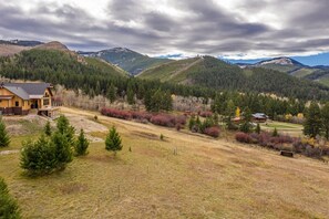 Eine Hütte mit einer Terrasse, umgeben von bewaldeter Landschaft und sanften Hügeln.