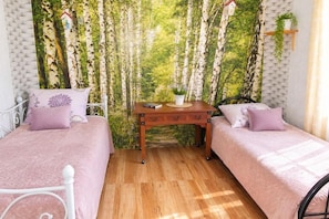 Ein Zimmer mit zwei Betten, einem Holztisch und einem Wandgemälde mit Bäumen.
