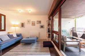 Un salon moderne avec un canapé, un pouf et une porte vitrée donnant sur un espace de détente extérieur.