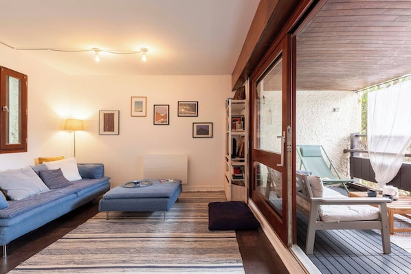 Ein modernes Wohnzimmer mit Sofa, Hocker und einer Glastür zu einem Sitzbereich im Freien.