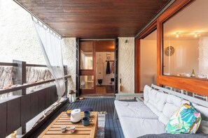Ein Balkon mit Holzboden, einer weißen Couch, einem Tisch mit Teekanne und Tassen sowie Blick ins Zimmerinnere.
