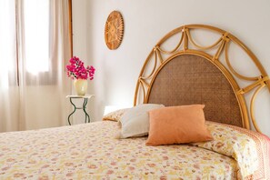 A bed with a floral bedspread, a round woven headboard, and a vase with pink flowers on a small table beside the bed. - Agro Antico B B Queen Room Morgana (Syracuse)