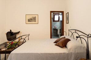 Ein Schlafzimmer mit einem Bett, einem Nachttisch mit einer Handtasche, einem gerahmten Bild an der Wand und einer Badezimmertür.