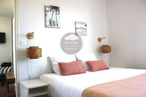 Habitació d'hotel amb llit, una taula de nit, una làmpada penjada a la paret i una fotografia emmarcada.