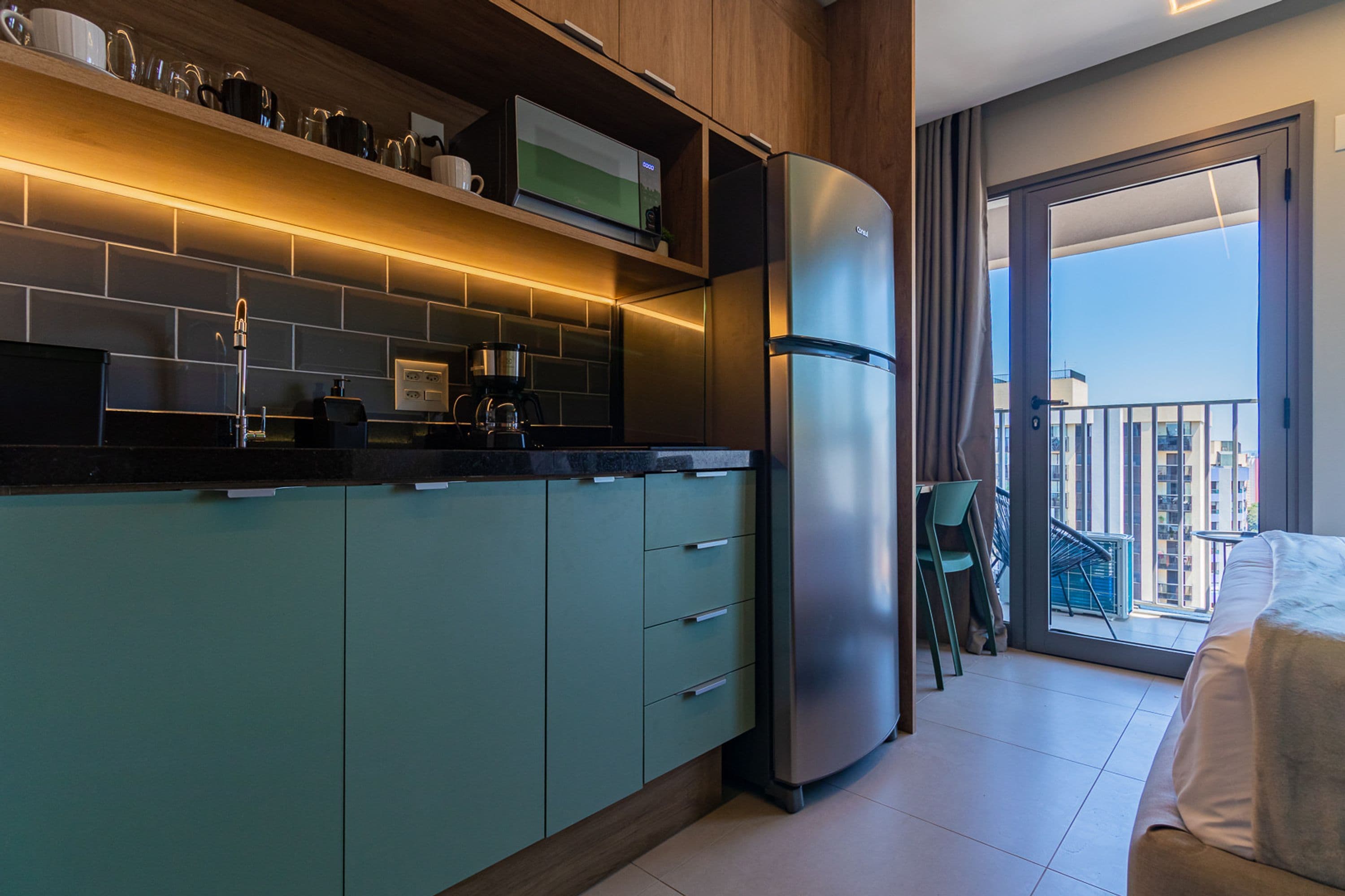 A modern kitchen with a built-in refrigerator, a coffee maker, and a microwave. There is a balcony with a view of the city.