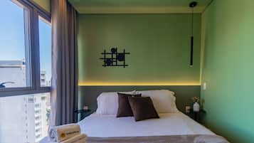 A hotel room with a bed, a nightstand, a wall-mounted light fixture, and a window with curtains.