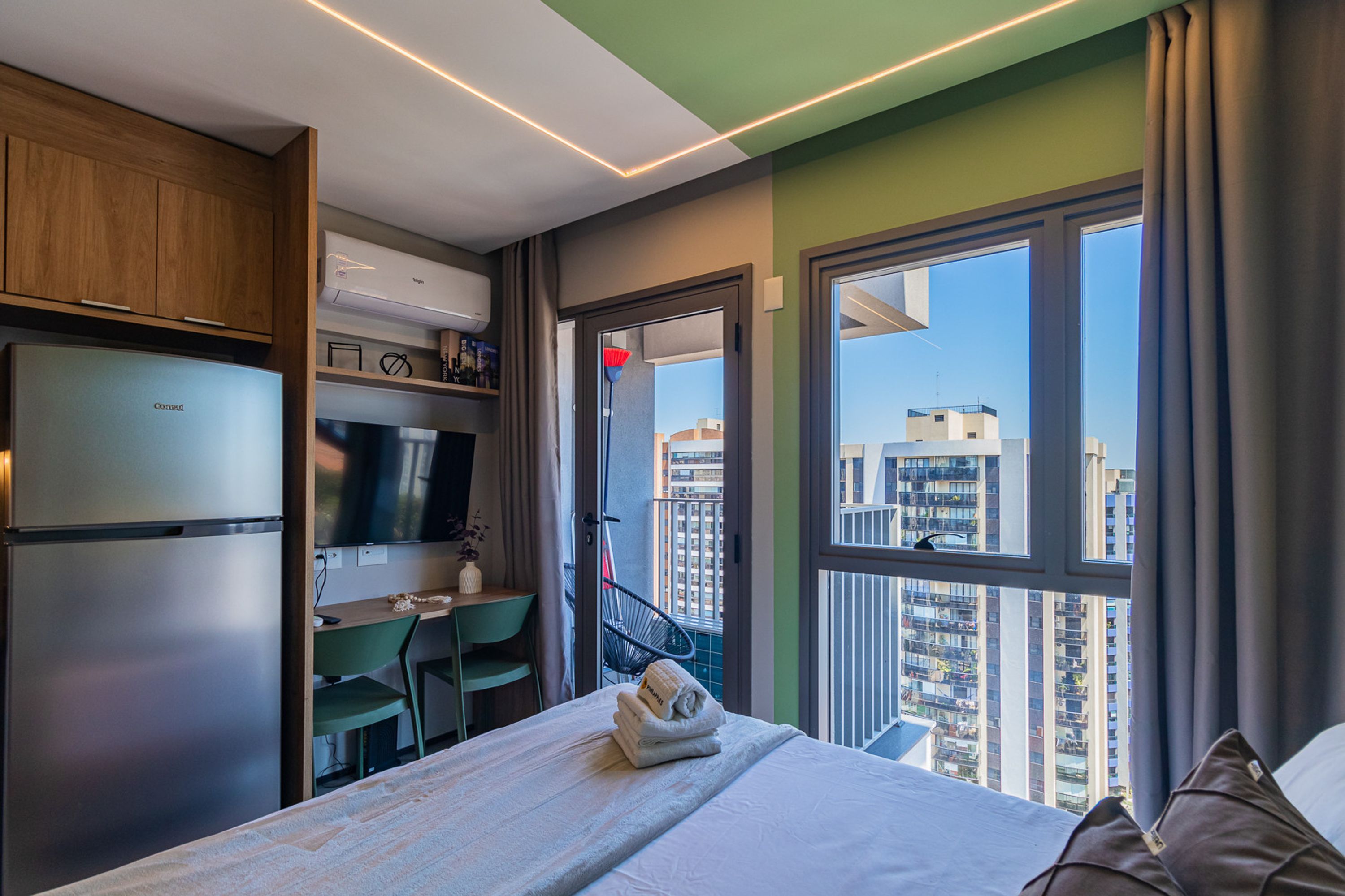 A hotel room with a bed, a desk, a television, and a view of the cityscape.