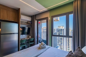 Une chambre d’hôtel équipée d’un lit, d’un bureau, d’une télévision et offrant une vue sur le paysage urbain.