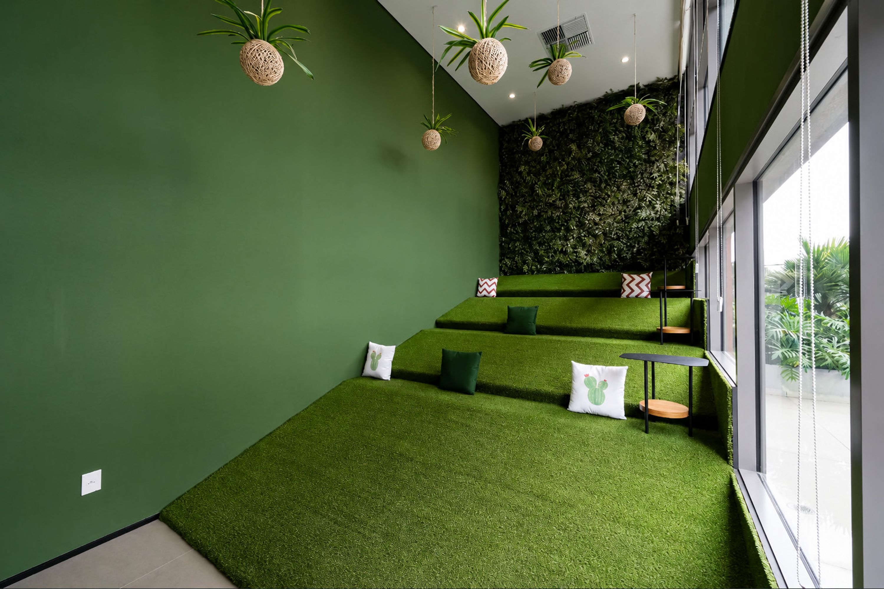 A room with green walls, a green carpet, and a green wall with a textured pattern. There are pillows on the carpet and a small table with a chair.