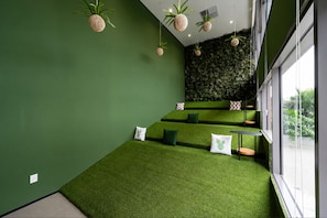 Une pièce aux murs verts, avec un tapis vert et un mur vert orné d’un motif texturé. On y trouve des coussins sur le tapis et une petite table avec une chaise.
