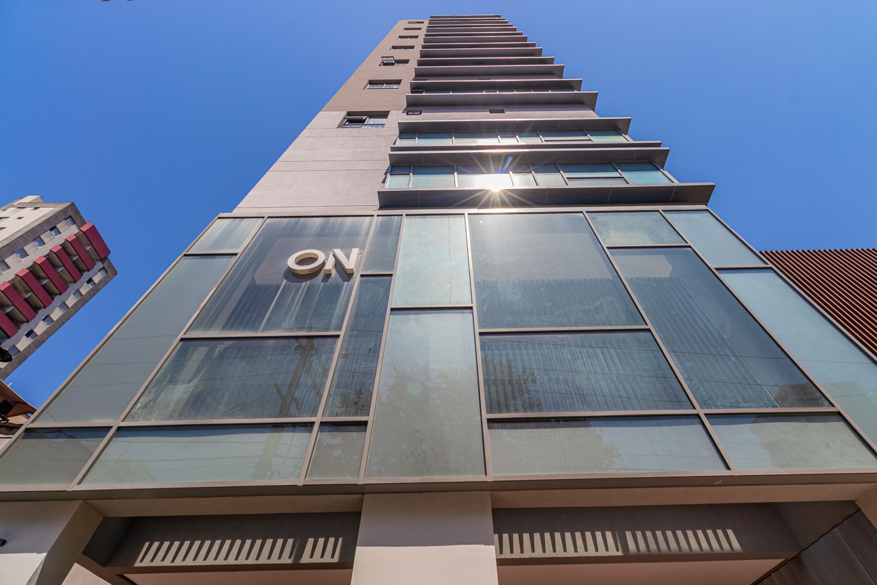 A modern building with a prominent 'ON' sign on the facade, large windows, and a clear blue sky in the background.