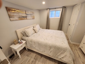 Une chambre à coucher avec un lit, une table de chevet, une fenêtre avec des rideaux et une porte.