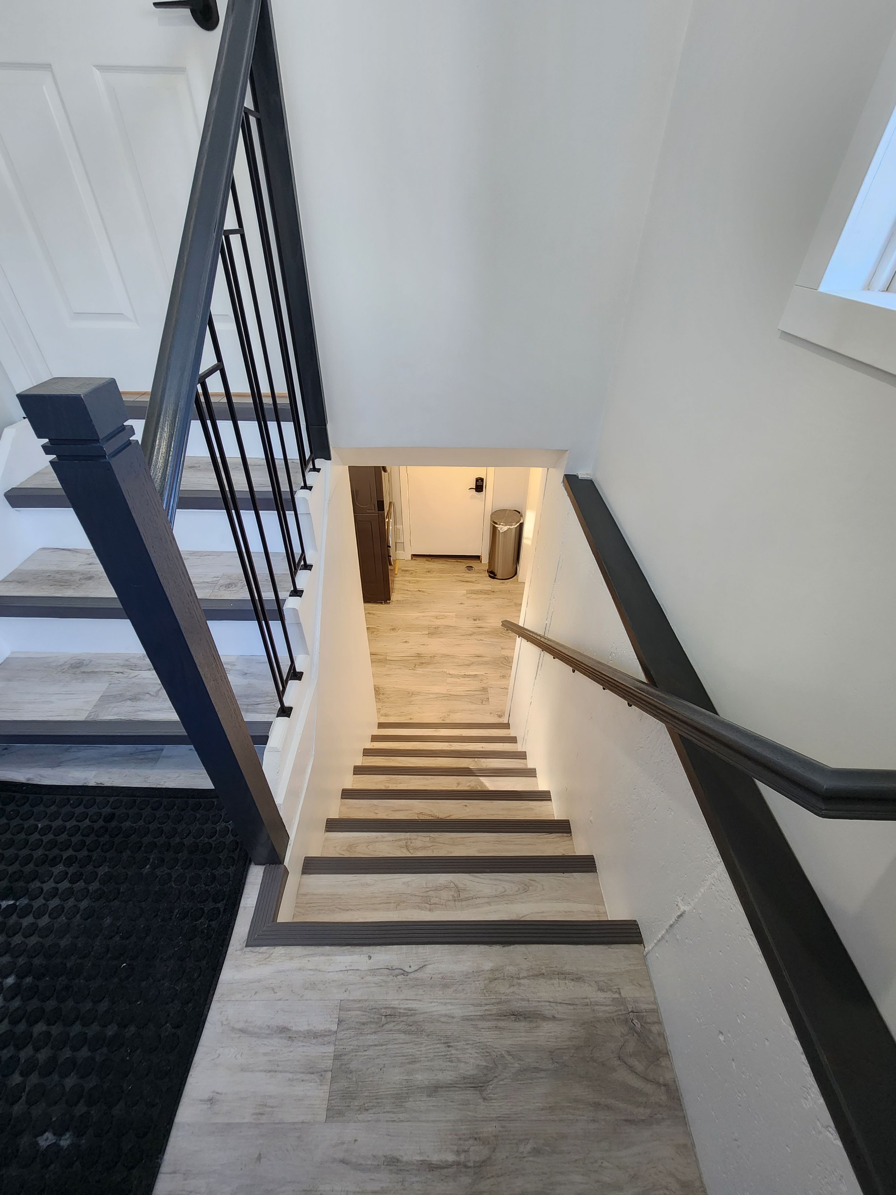 A modern staircase with a handrail, leading to a room with a wooden floor and a door.