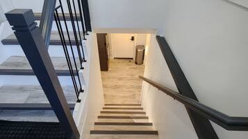 A modern staircase with a handrail, leading to a room with a wooden floor and a door.