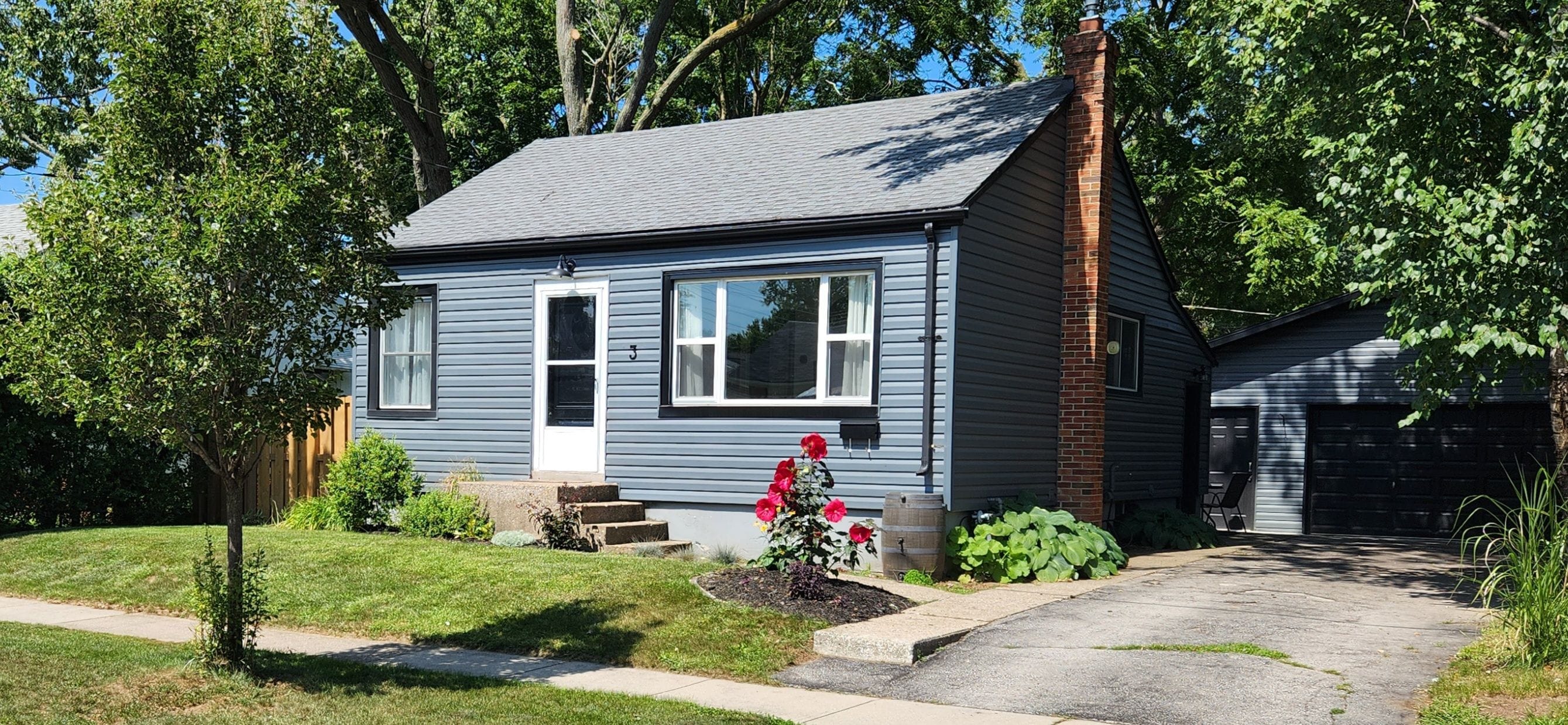A two-story house with a grey exterior, a front porch, and a small garden with red flowers.