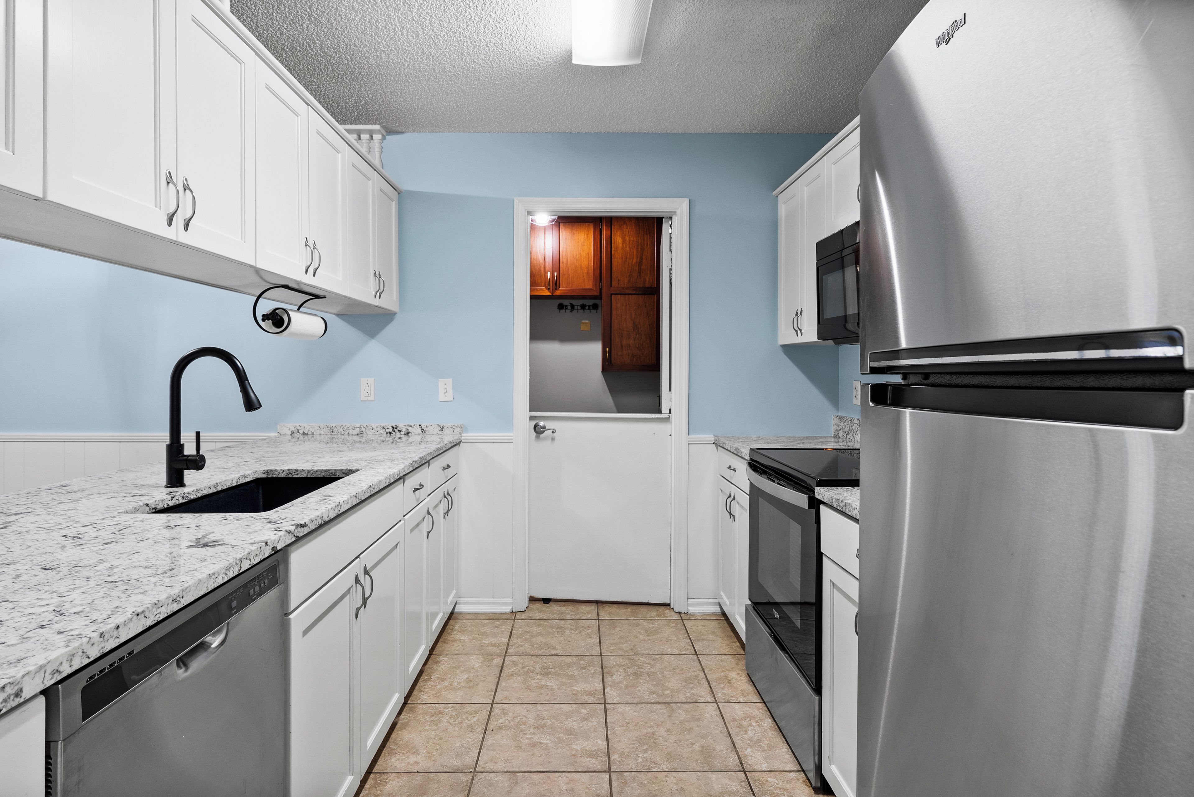 A kitchen with white cabinets, a stainless steel refrigerator, a microwave, a dishwasher, and a granite countertop.