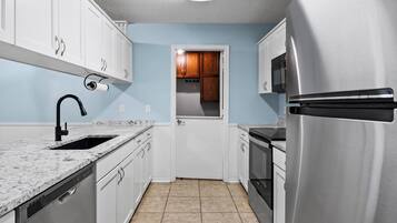 A kitchen with white cabinets, a stainless steel refrigerator, a microwave, a dishwasher, and a granite countertop.