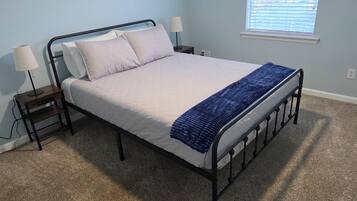 A bedroom with a bed, a ceiling fan, a nightstand, a lamp, and a window with blinds.