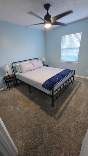 A bedroom with a bed, a ceiling fan, a nightstand, a lamp, and a window with blinds. - 3-bedroom duplex with 2 living rooms, close to Tiger Town and I85 (Opelika)