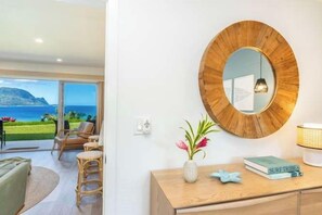 A room with a round mirror, a wooden desk, a vase with flowers, and a book titled 'SURF TRIPS'. - Pali Ke Kua 124 - Bali Hai View, Beautiful Ocn Frt condo (Princeville)