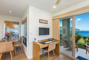 A modern room with a dining area, a flat-screen TV, and a large sliding glass door leading to a balcony with a view of the sea. - Pali Ke Kua 124 - Bali Hai View, Beautiful Ocn Frt condo (Princeville)