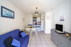 A compact living space with a kitchenette, a dining area, and a seating area with a blue sofa. - La Parenthèse de Pentrez - 100 m de la plage (Saint-Nic)