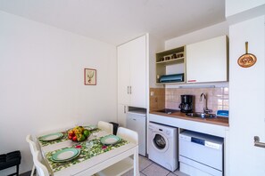 A compact kitchen with a dining area, a washing machine, and a coffee maker. - La Parenthèse de Pentrez - 100 m de la plage (Saint-Nic)