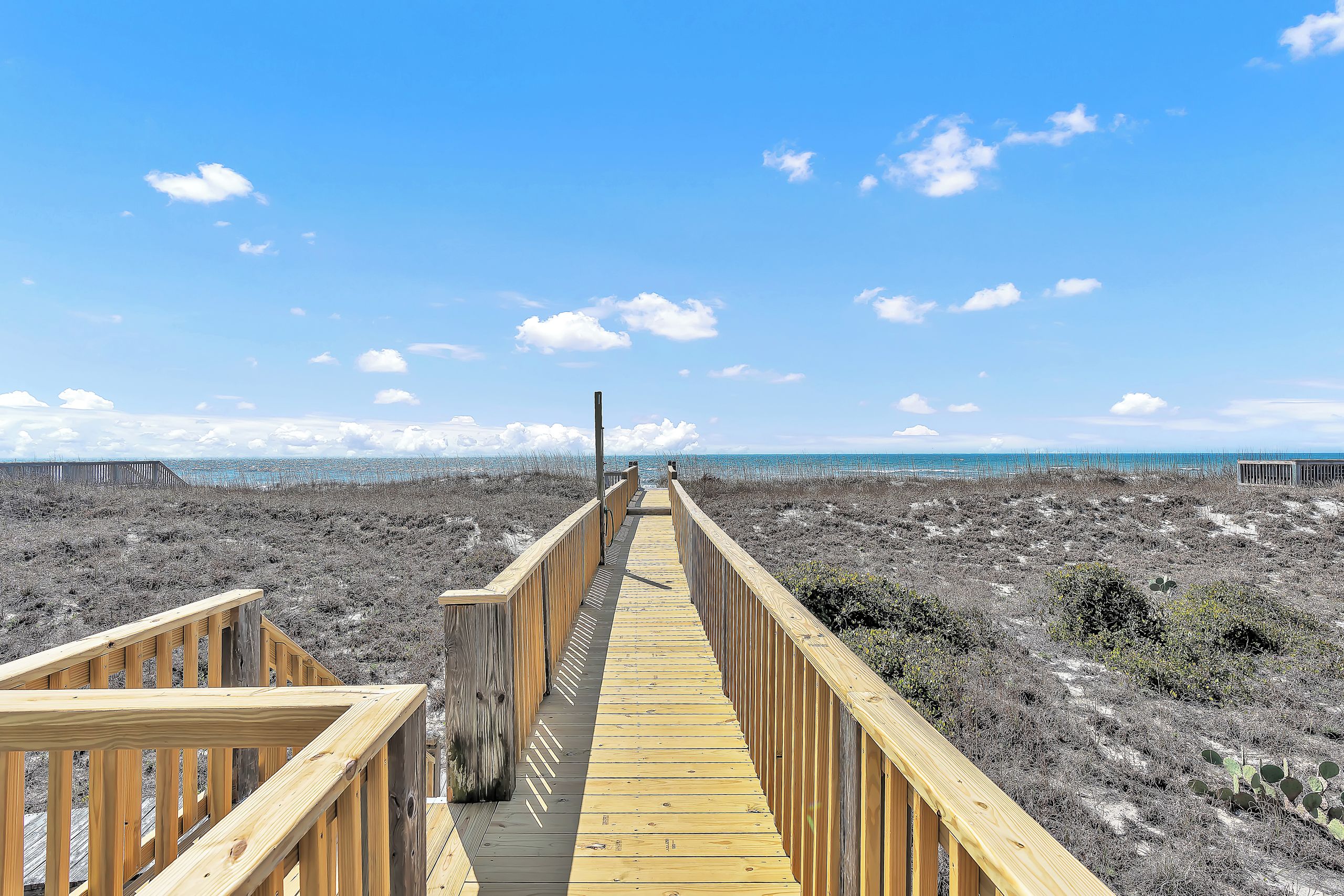 A wooden boardwalk leading to a beach with a clear sky.