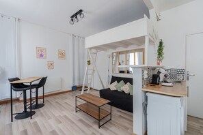 A compact living space with a kitchenette, a dining area with a table and chairs, a black sofa, and a ladder against the wall. - Le Saint Lambert - studio au cœur de Troyes (Troyes)