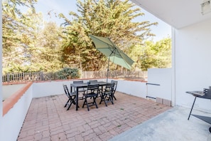 Eine Terrasse im Freien mit Tisch, Stühlen, einem Grill und einem großen Sonnenschirm.