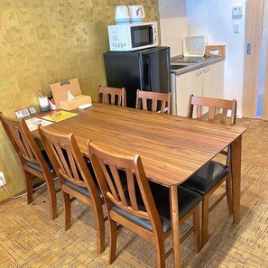 A dining area with a wooden table and chairs, a microwave, a refrigerator, and a small kitchenette. - One More Heart Kyoto Station South 5 (Kyoto)