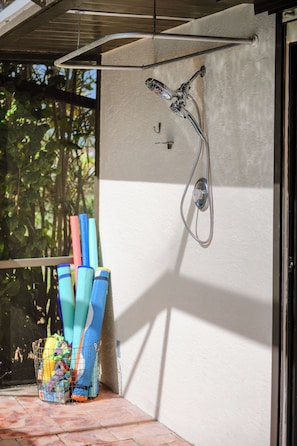 Un espace extérieur abrité, équipé d’une douche, d’une fenêtre et d’une collection de tapis colorés.