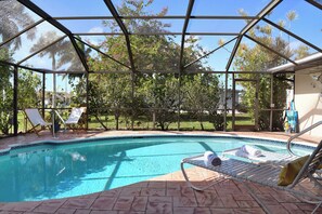 Ein überdachter Pool mit Liegestühlen und Blick auf Bäume.